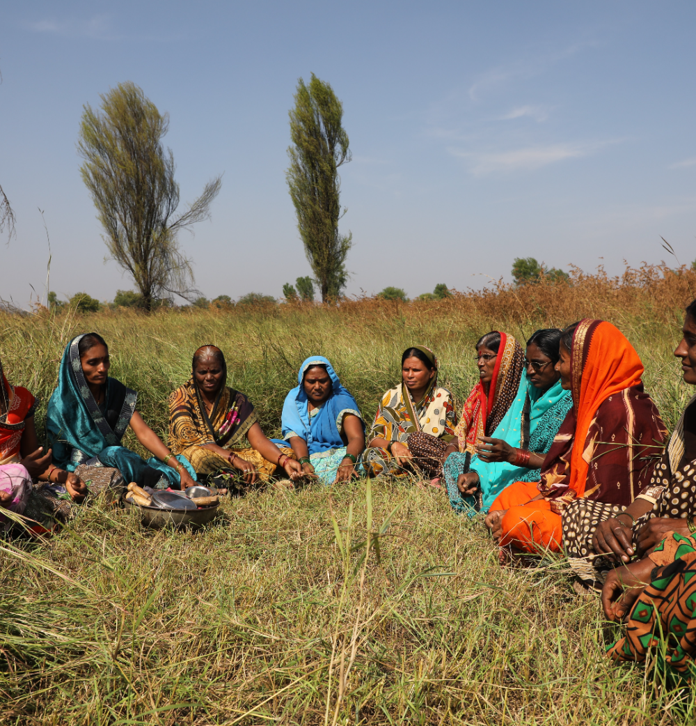 A women's collective in group discussion in a field during a community study